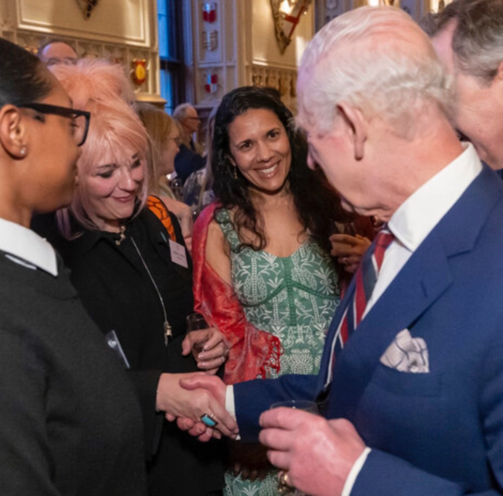 A group of people engaging in conversation and shaking hands during a community music event at Windsor Castle, featuring King Charles III.